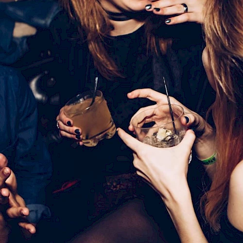 A group of people enjoying drinks and conversation in a social setting, holding cocktails with straws while sharing a laugh and interacting closely.