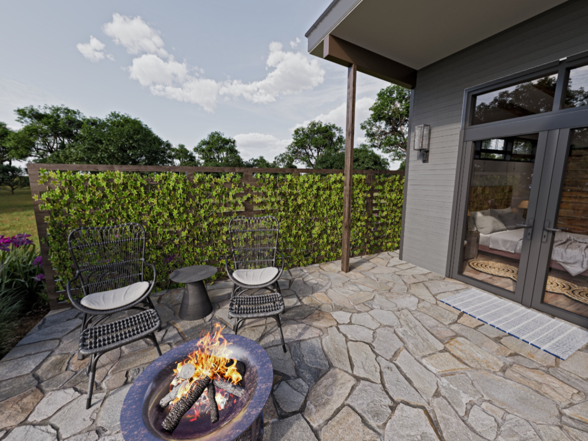 The image shows an outdoor patio with a fire pit, three chairs, and a small table. There's also a stone path and a green wall in the background.