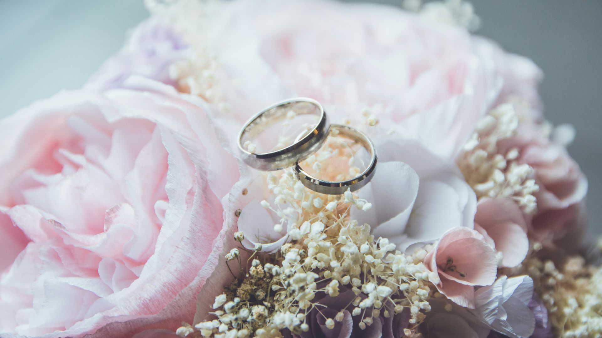 Two wedding rings rest atop a delicate bouquet of pale pink and white flowers, symbolizing love and commitment in a beautiful setting.