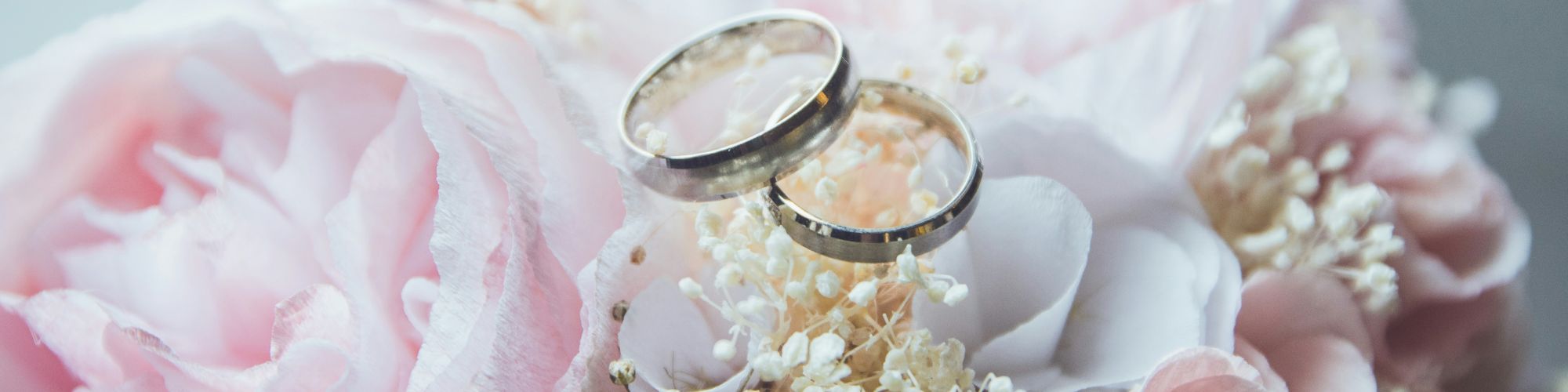 Two wedding rings rest atop a delicate bouquet of pale pink and white flowers, symbolizing love and commitment in a beautiful setting.